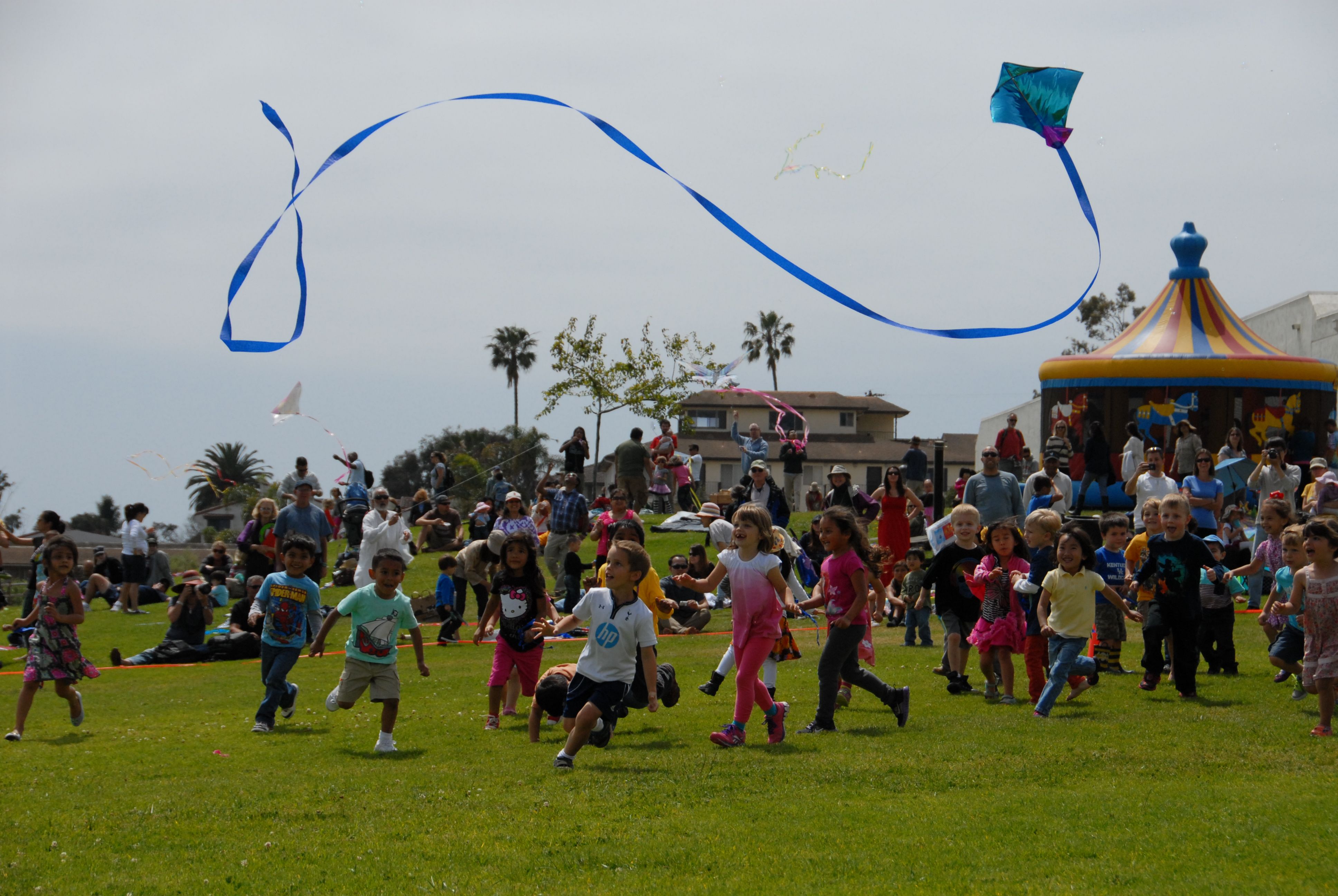 Children running on a large green lawn, chasing the tail of a kite
